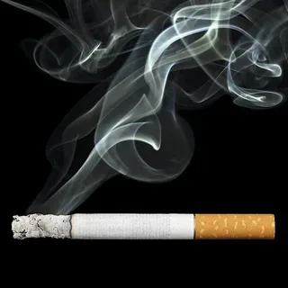 Lit cigarette with smoke curling up against a black background