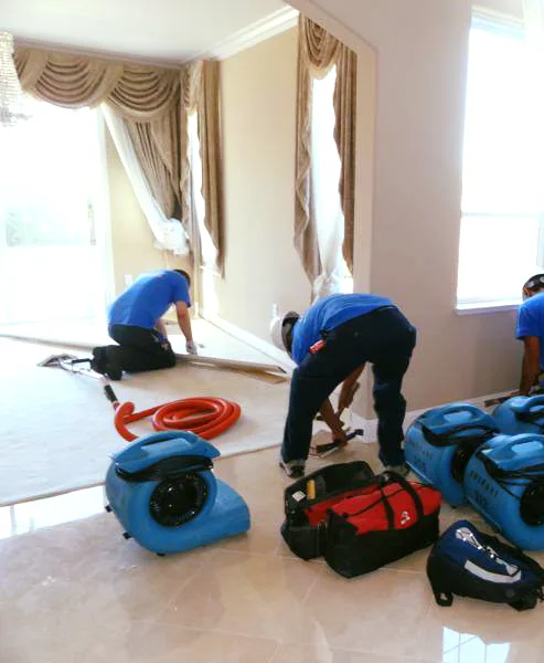 Restoration crew pulling back wet flooring and setting up air movers in a Memphis home