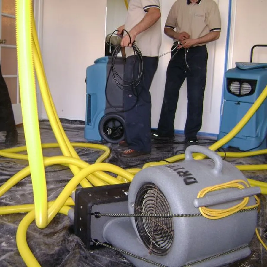 Technicians setting up dehumidifiers, an air mover and drying hoses in a room during water mitigation