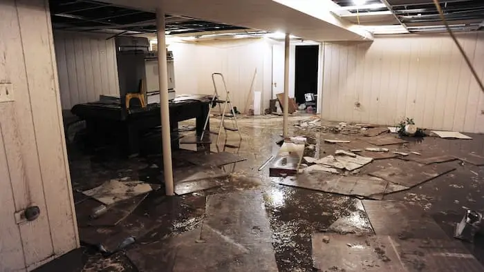 Finished basement with fallen ceiling tiles, debris and standing water across the floor