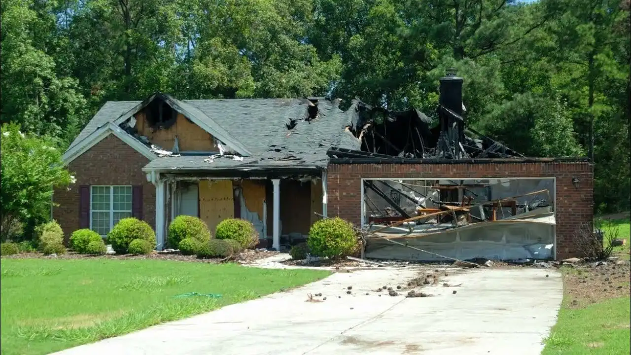 Brick house with a burned-out roof and garage after a house fire, front windows boarded up