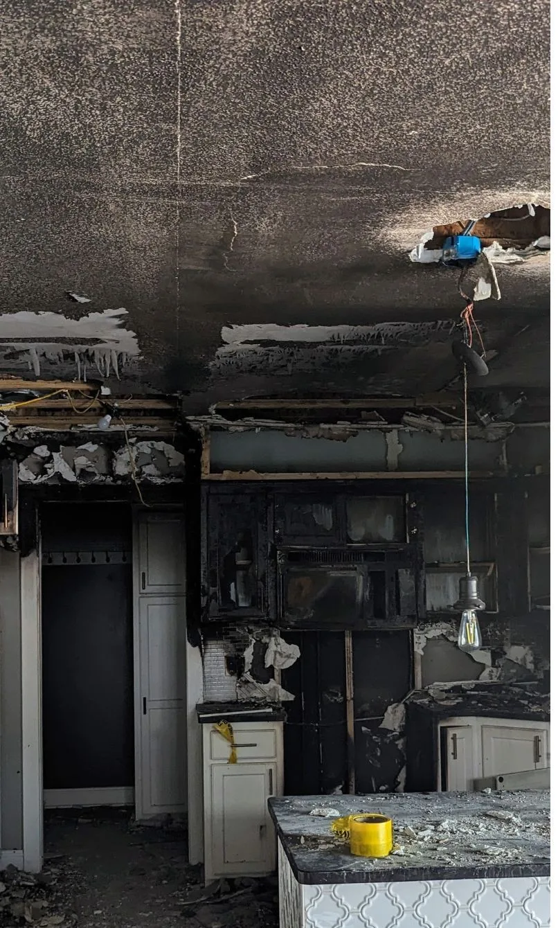 Kitchen after a fire, with a soot-blackened ceiling and cabinets and burned debris on the counter