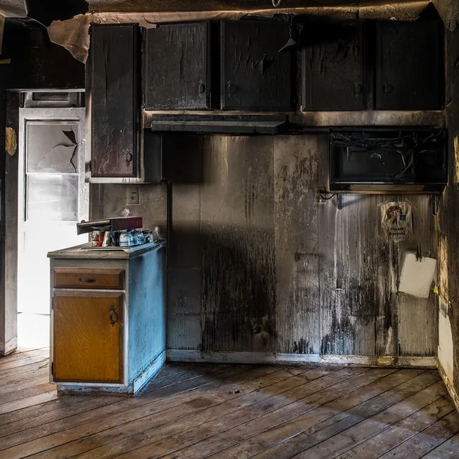 Kitchen after a small fire, with smoke-blackened cabinets, range hood and walls streaked with soot