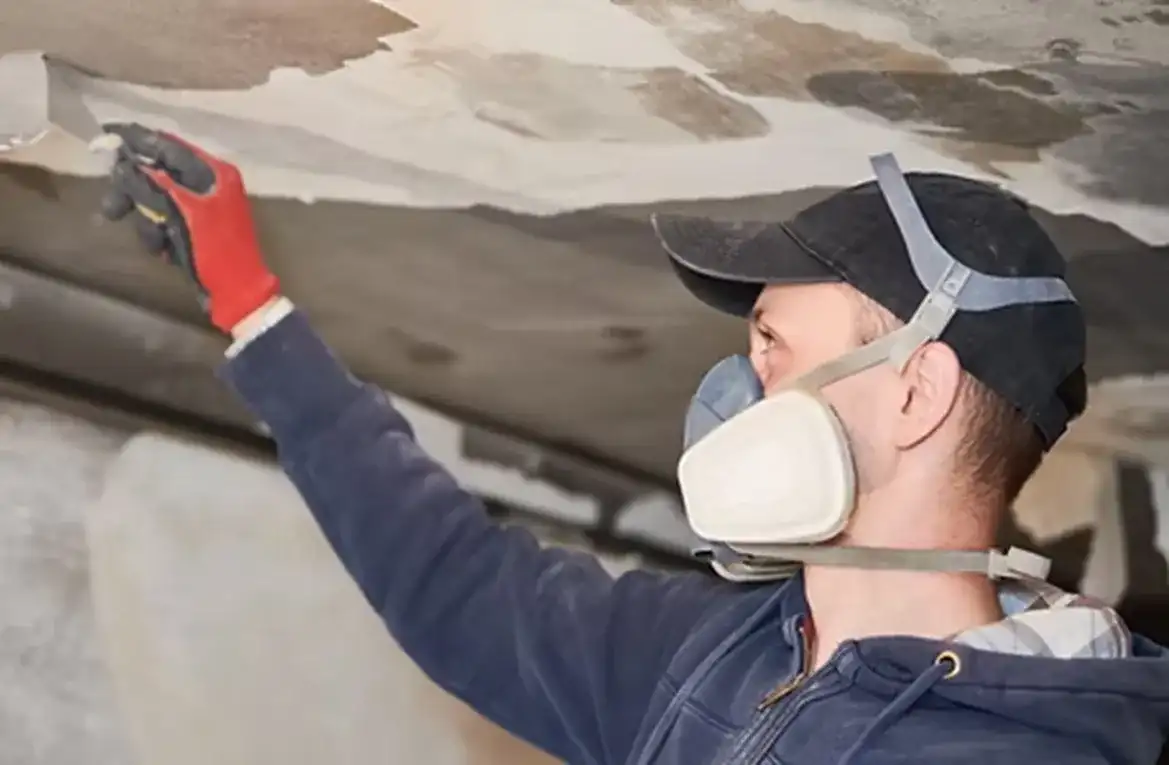 Worker in a respirator and gloves cleaning a smoke-damaged ceiling