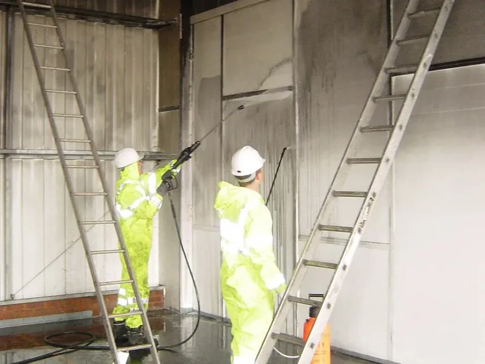 Two workers in protective suits washing soot off the walls of a commercial building