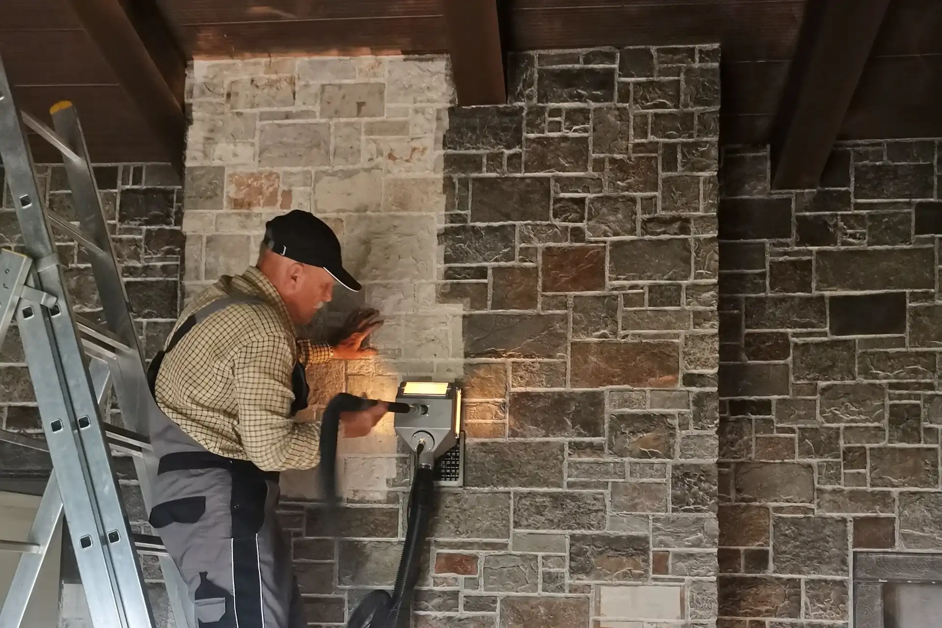 Worker cleaning dark residue off an indoor stone wall, with the cleaned stone much lighter