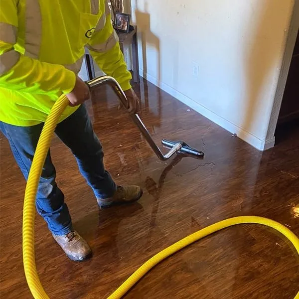 Technician extracting standing water from a hardwood floor with a wand and hose