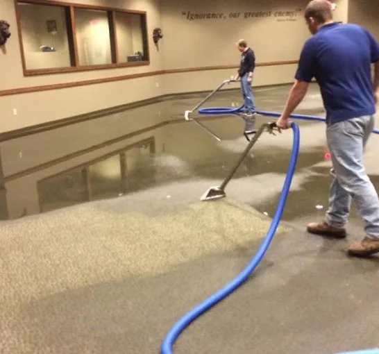 Two technicians extracting standing water from a flooded commercial floor with extraction wands